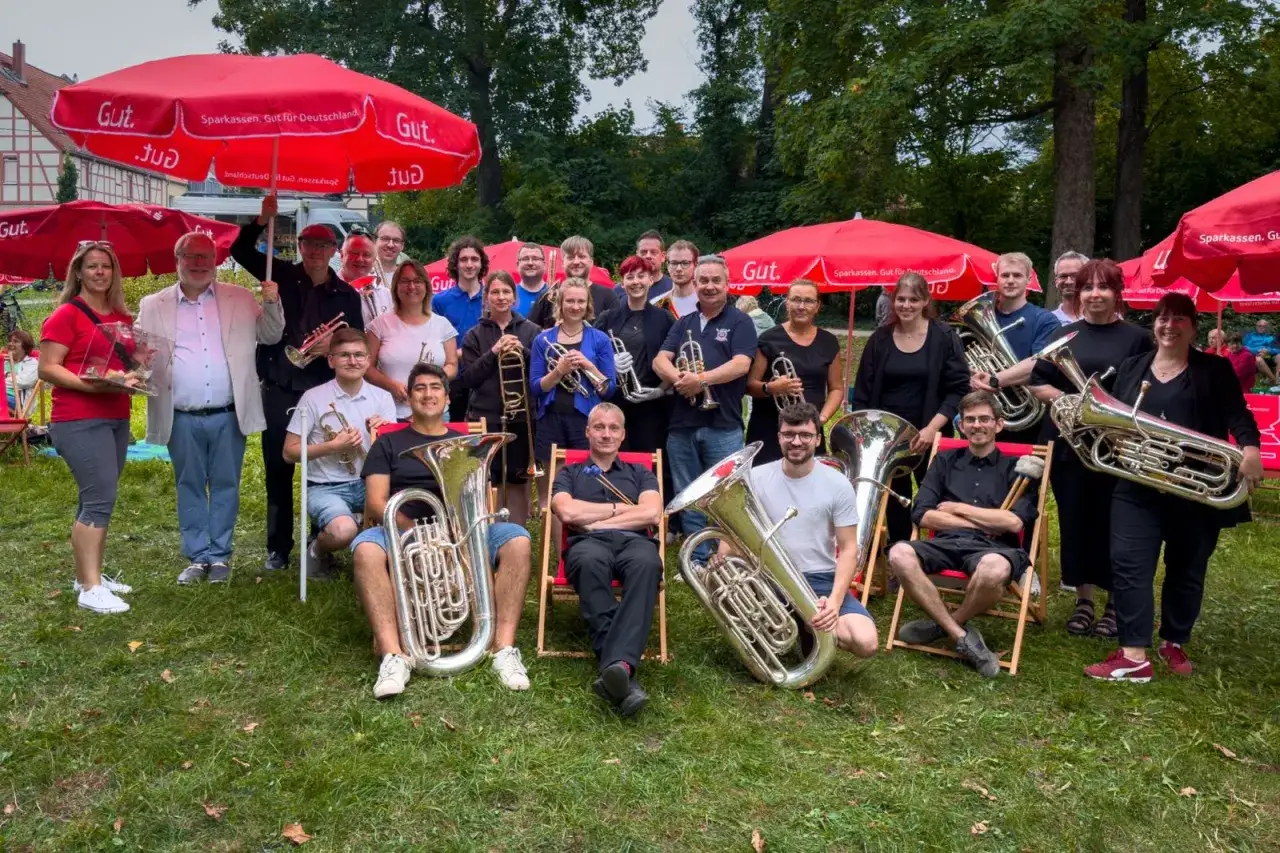 Eine fr&ouml;hliche Brass Band posiert unter roten Sonnenschirmen. Viele Mitglieder halten ihre Instrumente, bereit f&uuml;r ein Konzert.