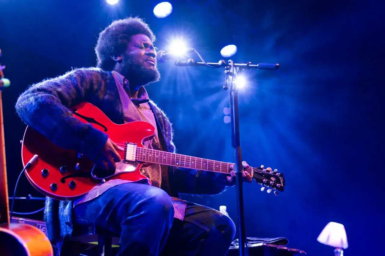 Michael Kiwanuka spielt leidenschaftlich seine rote E-Gitarre unter blauem Bühnenlicht.