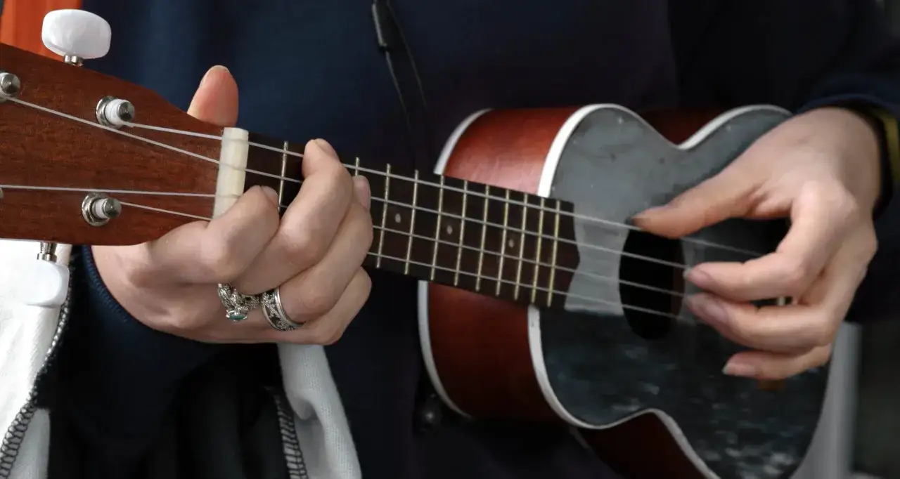 Hände spielen auf einem Ukulele, einem kleinen Saiteninstrument.