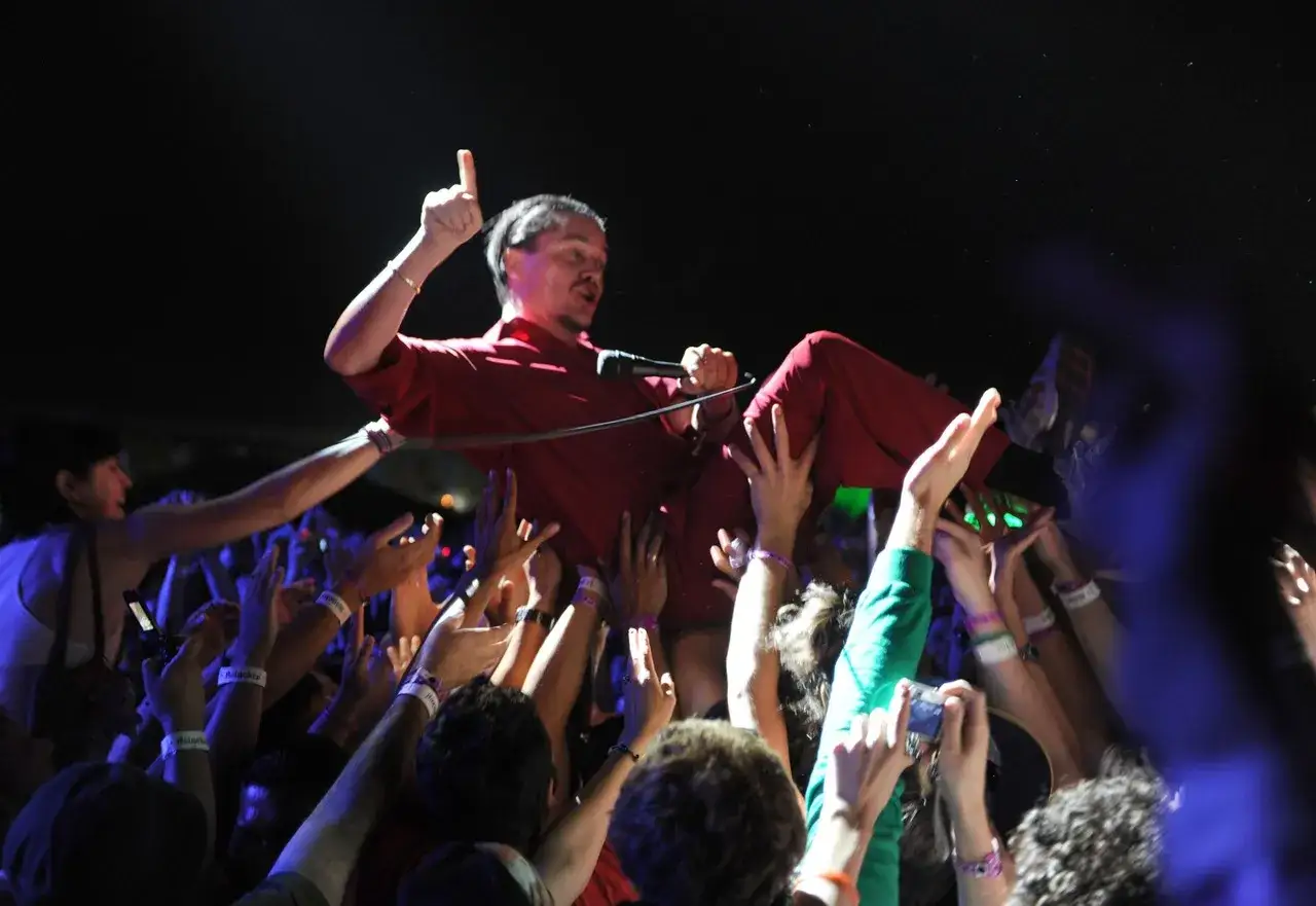 Mike Patton heute: Der Sänger wird von der Menge getragen, Mikrofon in der Hand, ein Finger zeigt nach oben.