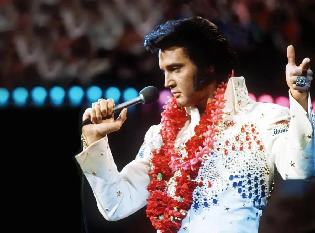 Elvis Presley, mit einer Blumenkette, singt auf der Bühne. Ein ikonischer Moment von Elvis Hawaii.