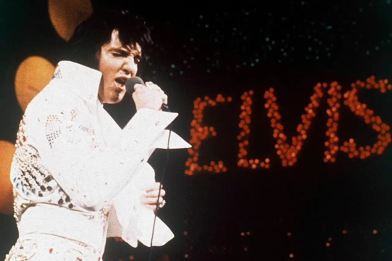 Elvis Presley singt in seinem berühmten weißen Anzug in Las Vegas. Der Schriftzug