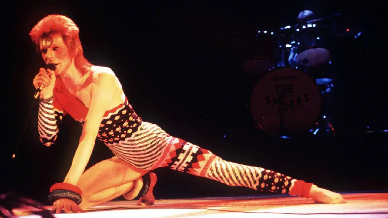 David Bowie in einem extravaganten Outfit auf der B&uuml;hne, die Energie der Drogen und des Rock'n'Roll in seiner Performance.