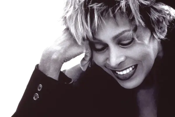Tina Turner lächelt mit geschlossenen Augen, die Hand am Kopf. Ein ikonisches Bild der Musiklegende.