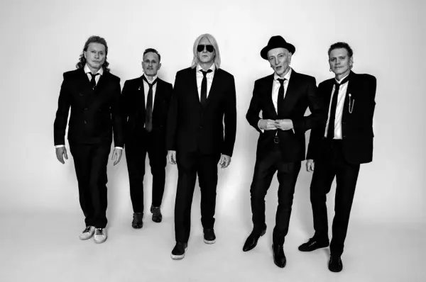 Fünf Männer in schwarzen Anzügen und Krawatten, die wie der titel von Def Leppard aussehen, posieren für ein Schwarz-Weiß-Foto.